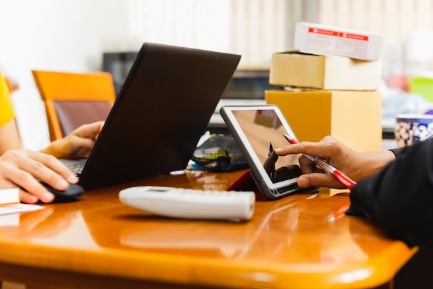 Geschäftsleute, die auf Tablette von zu Hause mit Postpaket auf Tisch arbeiten.