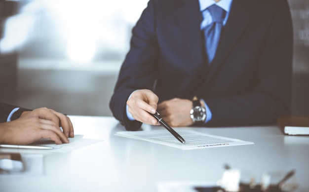 Geschäftsleute, die einen Vertrag besprechen, bei Besprechungen zusammenarbeiten, am Schreibtisch in einem modernen Büro sitzen. Unbekannter Geschäftsmann mit einem Kollegen oder Anwälten bei Verhandlungen. Teamarbeit und Partnerschaft co