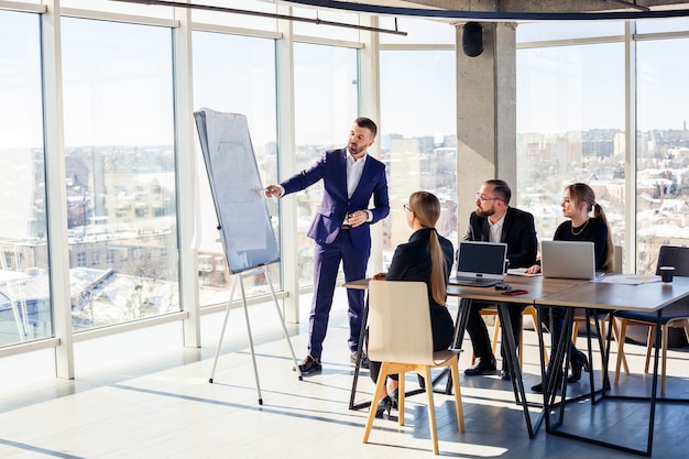 Geschäftsleute, die in einem modernen Büro mit Blick auf das Stadtbild zusammenarbeiten. Der Direktor informiert die Mitarbeiter über neue Technologien. Büroarbeitskonzept