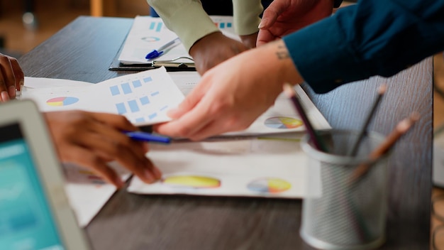 Geschäftsleute, die sich Diagramme und Diagramme auf Dokumenten ansehen und Forschungsinformationen auf Papieren analysieren, um eine Büropartnerschaft zu planen. Kollegen, die Dateninfografikdateien verwenden. Nahansicht.