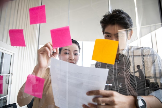 Geschäftsleute, die sich im Büro treffen, verwenden Notizen auf einer klaren Tafel, um Ideen bei der Arbeit im Besprechungsraum zu teilen.