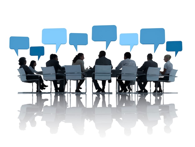 Geschäftsleute diskutieren um den Konferenztisch und Sprechblasen über ihnen.