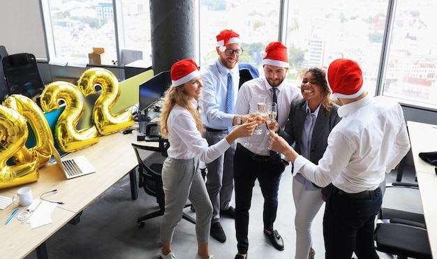 Geschäftsleute feiern Urlaub im modernen Büro, trinken Champagner und haben Spaß beim Coworking. Frohe Weihnachten und ein gutes neues Jahr 2022.