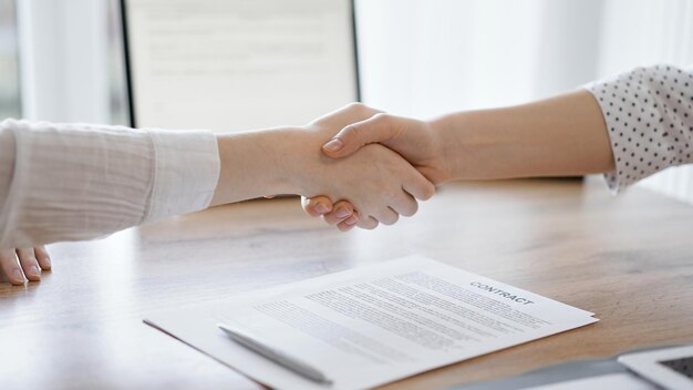 Geschäftsleute schütteln sich die Hände über den Vertragsunterlagen, die gerade auf dem Holztisch unterzeichnet wurden, aus nächster Nähe. Anwälte bei Treffen. Teamarbeit, Partnerschaft, Erfolgskonzept.