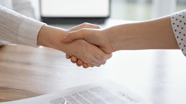 Geschäftsleute schütteln sich die Hände über Vertragspapieren, die gerade auf dem hölzernen Tisch unterzeichnet wurden, in der Nähe. Anwälte bei einem Treffen. Teamwork, Partnerschaft, Erfolgskonzept.