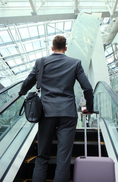 Geschäftsmann am Flughafen, der die Rolltreppe hinunterfährt.