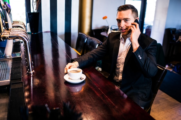 Geschäftsmann am Telefon, das einen Kaffee am Zähler in einer Bar trinkt