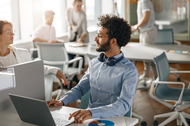 Geschäftsmann arbeitet am Laptop, während er im modernen Büro auf dem Hintergrund der Kollegen sitzt