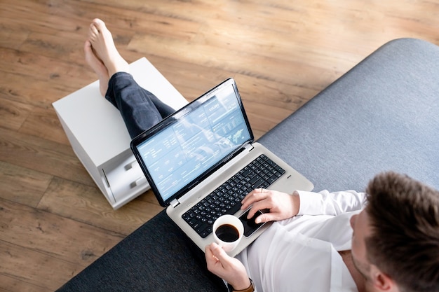 Geschäftsmann bei der Arbeit. Ansicht des Mannes, der am Laptop beim Sitzen an der Couch arbeitet