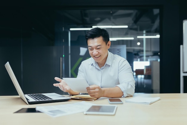 Geschäftsmann bei der Arbeit asiatischer Mann, der einen guten Brief von der Bank über die Eröffnung einer Kreditlinie liest