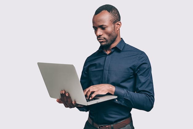 Geschäftsmann bei der Arbeit. Schöner junger Afrikaner, der im Stehen am Laptop arbeitet