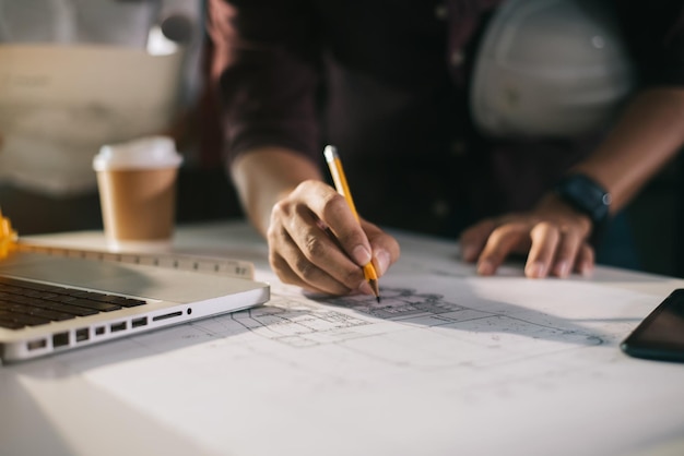 Geschäftsmann, der als Team arbeitet und über Datenarbeit und Tablet-Laptop mit einem Architekturprojekt auf der Baustelle am Schreibtisch im Büro diskutiert