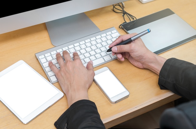 Geschäftsmann, der am Arbeitsplatz mit Computer, Tablette, intelligentem Telefon, Schlüsselbrett und Kaffee arbeitet