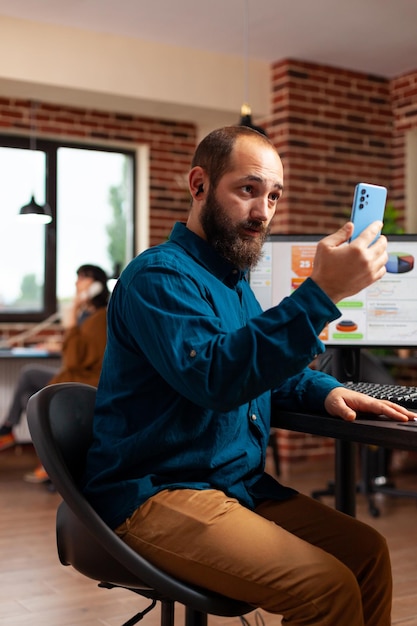 Geschäftsmann, der am Schreibtisch sitzt und Smartphone liest E-Mail-Nachrichten mit einem entfernten Freund, der gute Nachrichten erzählt, während er am Managementprojekt arbeitet. Manager, der nach Geschäftsinformationen sucht