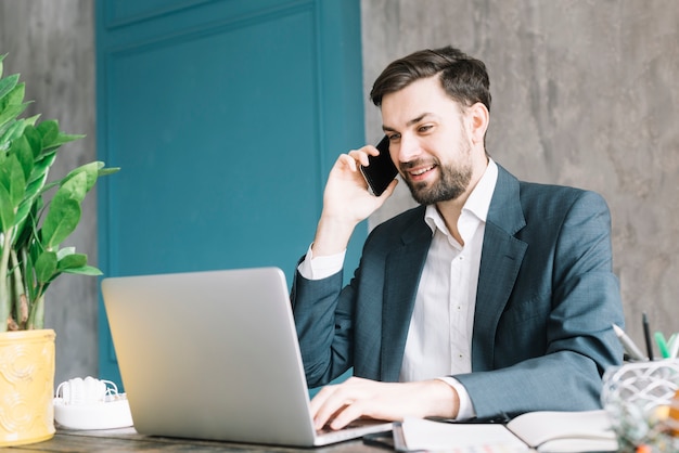 Geschäftsmann, der am Telefon nahe Laptop spricht