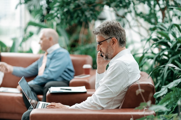 Geschäftsmann, der auf einem Smartphone spricht und an einem Laptop arbeitet