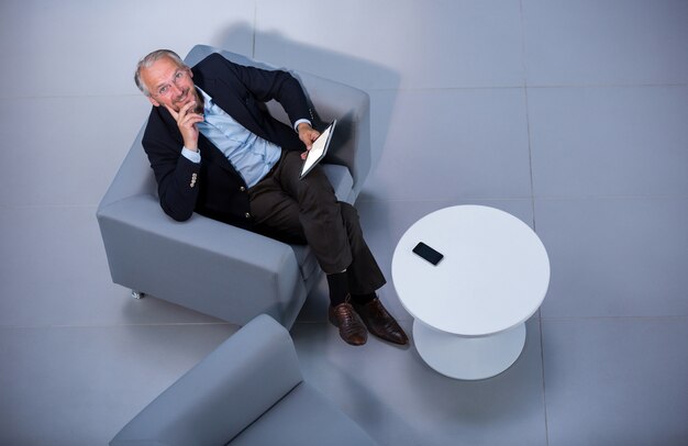 Geschäftsmann, der auf Stuhl mit digitaler Tablette im Büro sitzt