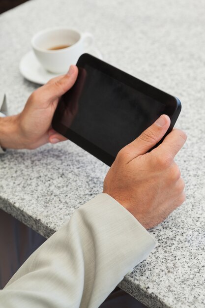 Geschäftsmann, der bei Tisch einen kleinen Tabletten-PC verwendet