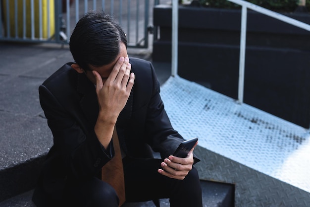 Geschäftsmann, der das Telefon benutzt, während er auf der Treppe sitzt. Verärgerter umgekippter Geschäftsmann, der das Telefon verwendet.