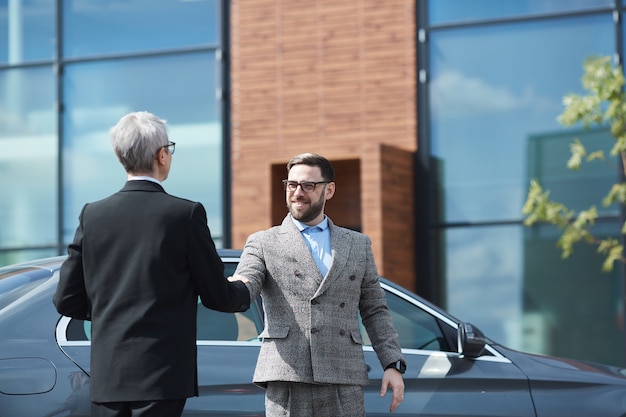 Geschäftsmann, der der Geschäftsfrau die Hand schüttelt, während sie sich in der Nähe des Bürogebäudes treffen
