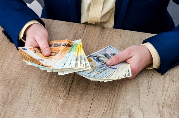 Geschäftsmann, der Dollar- und Euro-Banknoten hinter Holztisch zählt