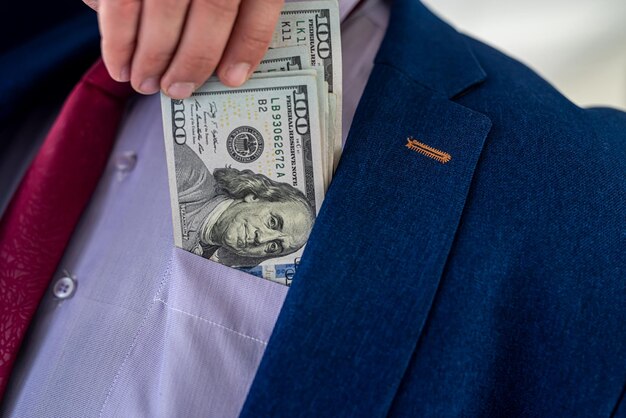 Geschäftsmann, der Dollargeld in seine Tasche steckt, wie nach einem erfolgreichen Geschäft oder einer Bestechung