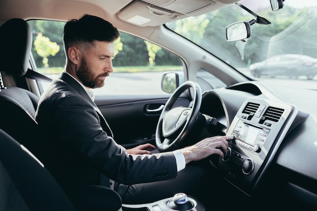 Geschäftsmann, der ein Auto fährt, schaltet die Musik im Autoplayer ein, ein Mann vor einer Reise in einem Business-Anzug