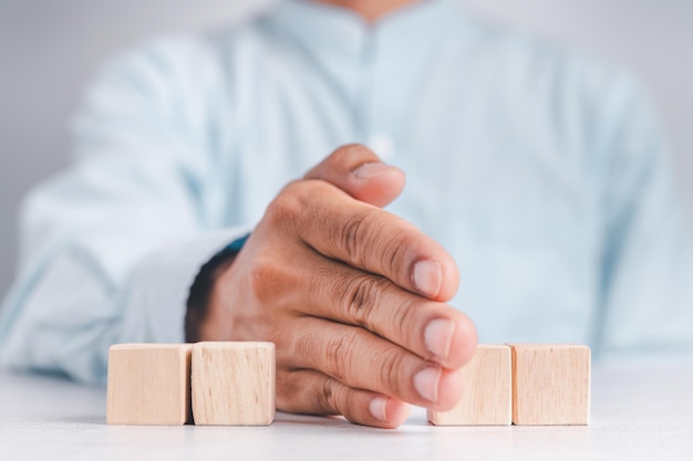 Geschäftsmann, der ein blaues Hemd trägt und die leeren Holzklötze mit seinen Händen anordnet, die auf einem weißen Holztisch platziert sind Geschäftsstrategie und Aktionsplan Kopierbereich