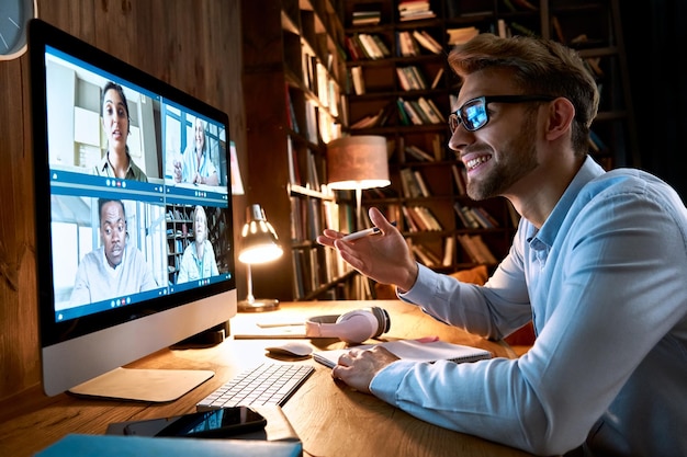 Geschäftsmann, der eine virtuelle Teamversammlung über einen Videokonferenzanruf mit Hilfe eines Computers durchführt Sozialdistanzarbeiter, der von zu Hause aus im Büro arbeitet, der mit verschiedenen Kollegen in einer Fernvideokonferenz im Online-Chat spricht