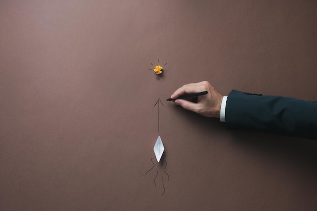 Geschäftsmann, der einen Pfeil in Richtung einer Glühbirne zeichnet, damit ein Origami-Papierschiff folgt