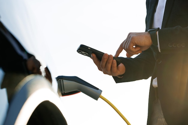 Geschäftsmann, der Elektroauto an einer Ladestation im Freien auflädt, nicht erkennbarer Mann, der einsteckt