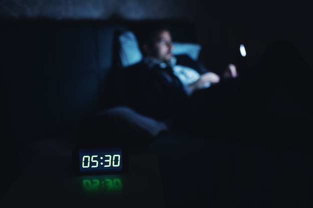 Geschäftsmann, der früh am Morgen auf dem Bett liegt und Tablette benutzt. Uhr zeigt 5:30. Selektiver Fokus auf die Uhr.