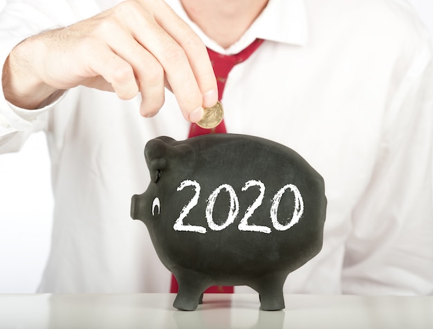 Geschäftsmann, der Geld auf ein Sparschwein mit einer Zeichnung des Jahres 2020 steckt