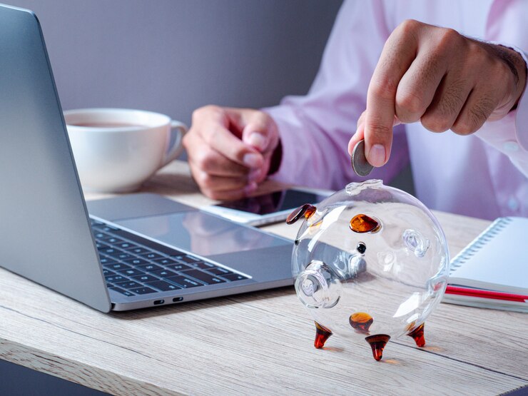 Foto geschäftsmann, der geldmünzen hält, die im sparschwein auf holztisch im büro setzen. sparen von geld für zukunftspläne und pensionsfonds, spar- und investitionsgelder für unternehmen oder finanzen