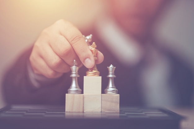 Geschäftsmann, der goldenes Königschach zur Siegerposition auf hölzernem Würfel des Schachspiels hält