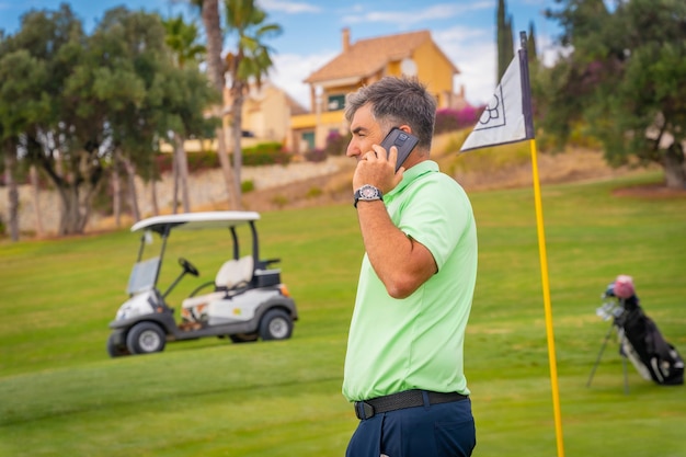 Geschäftsmann, der Golf spielt und einen Arbeitsanruf mit dem Telefon des Clubs beantwortet