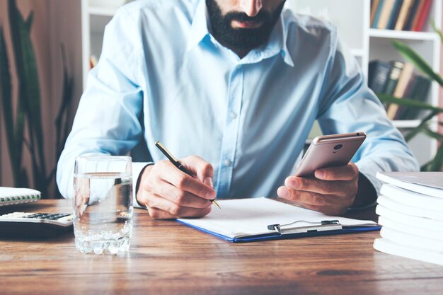 Geschäftsmann, der Handtelefon und Dokument arbeitet