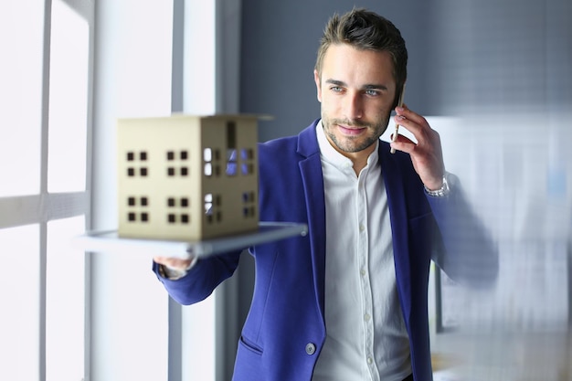 Geschäftsmann, der Hausminiatur auf der Hand hält, die im Büro steht