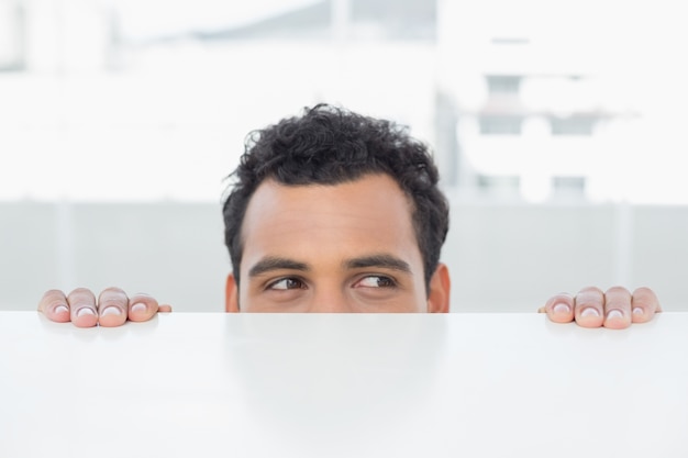 Geschäftsmann, der hinter den Schreibtisch im Büro späht