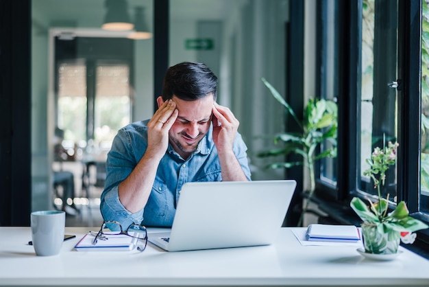 Geschäftsmann, der im Büro arbeitet und schmerzende Kopfschmerzen durch die Arbeit am Schreibtisch hat