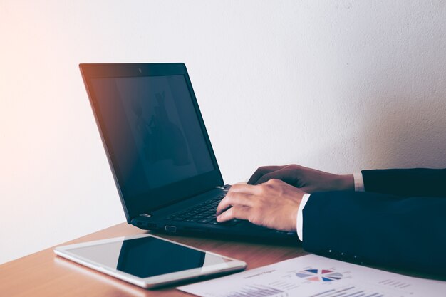 Geschäftsmann, der im Büro mit Laptop und Dokumenten auf seinem Schreibtisch arbeitet