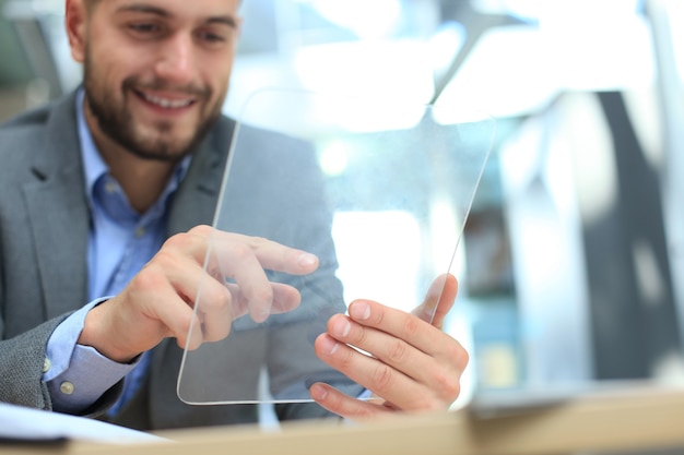 Geschäftsmann, der im Büro mit transparenter Tablette und Laptop arbeitet.