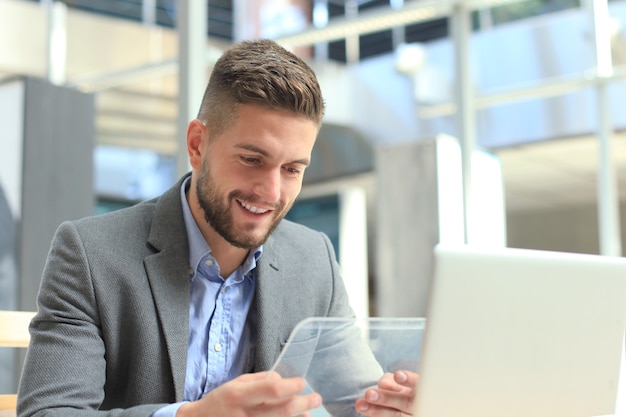 Geschäftsmann, der im Büro mit transparenter Tablette und Laptop arbeitet.