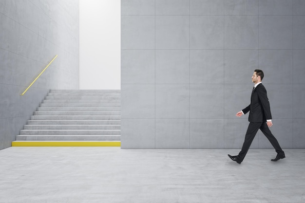 geschäftsmann, der in einem kreativen hellen betonflieseninnenraum mit treppen und mock-up-platz an der wand spazieren geht