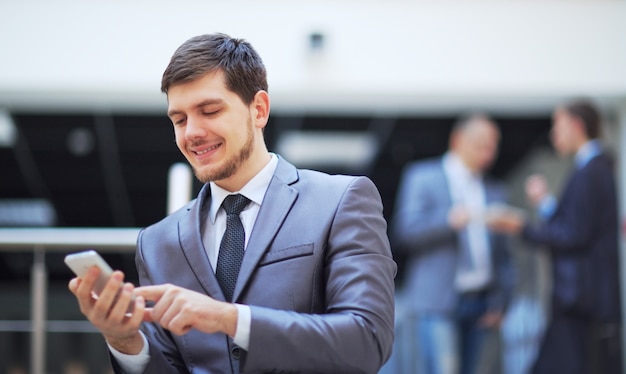 Geschäftsmann, der in einem modernen Bürogebäude steht und auf ein Mobiltelefon schaut