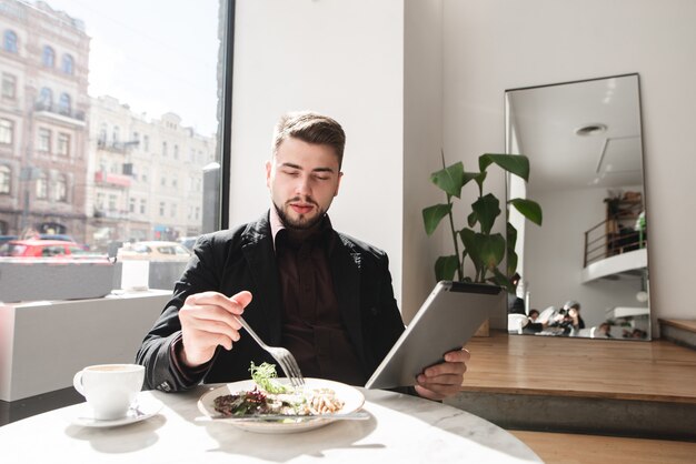 Geschäftsmann, der in einem Restaurant speist und eine Tablette verwendet.