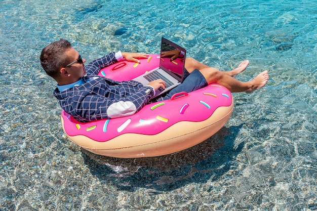 Geschäftsmann, der Laptop-Computer auf einem aufblasbaren Donut im Meer verwendet