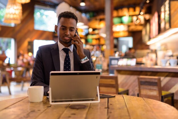 Geschäftsmann, der Laptop-Computer verwendet und am Telefon am Kaffeegeschäft spricht