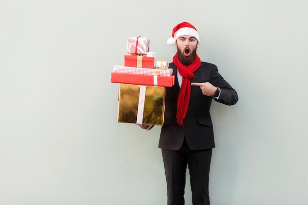 Geschäftsmann, der mit dem Finger auf viele bunte Geschenkboxen zeigt und mit offenem Mund und großen Augen schaut