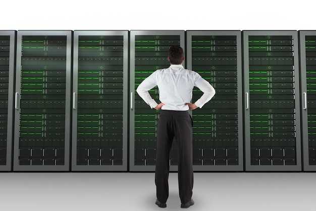 Geschäftsmann, der mit den Händen auf den Hüften gegen Servertürme zurück zur Kamera steht